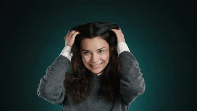 The girl is hysterically laughing, fixing her beautiful dark hair. She is on a dark, green-blue background. High quality 4k footage