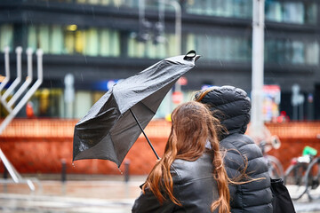 Ludzie pod parasolem w czasie deszczu i wiatru.  - obrazy, fototapety, plakaty