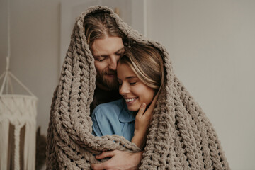 Beautiful young loving couple covering with a cozy warm blanket while spending time at home together