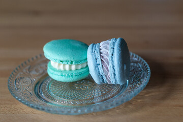 Two sweet French macaroons or meringue cookies on a small glass plate. The macaroons are blue and...