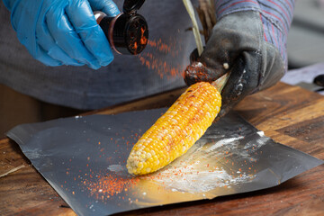 A sweet corn on the cob grilled on a barbeque with mayonnaise, cheese, butter, spices, and chili....