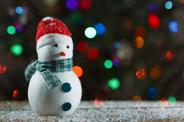 Snowman and Christmas tree. Winter home decorations. Holiday traditions and gifts. Merry Christmas. Snowman toy. Christmas tree lights bokeh on background. Fake snow on wooden desk. Happy New Year