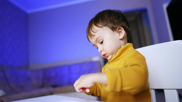 Focused little kid wearing yellow sweater dealing with felt pen. Baby boy getting ready to start drawing.