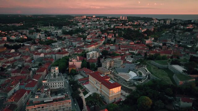 Flying above historic city of Pula at night with evening illumination, historic Roman amphitheatre of Pula aerial view, tourism in Croatia, vacations in the Adriatic.