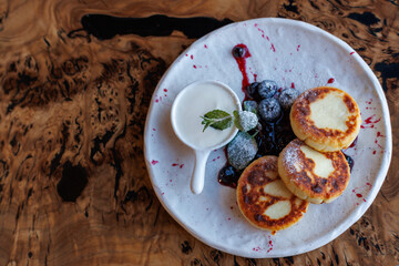 Cottage cheese fritters, ricotta pancakes or syrniki with sour cream yogurt on ceramic plate. Healthy calcium breakfast, lunch or snack. Traditional russian food. Wooden background, copy space