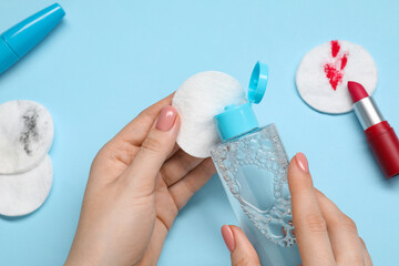 Woman using makeup remover, closeup. Cotton pads, lipstick and mascara on light blue background,...