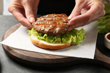 Woman making tasty hamburger with fried patty, lettuce and bun at table, closeup