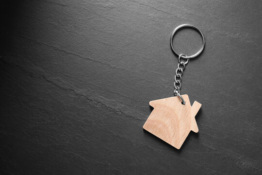 Wooden keychain in shape of house on dark textured table, top view. Space for text