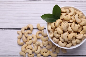 Tasty cashew nuts and green leaves on white wooden table, top view