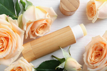 Lip balm and rose flowers on white wooden background, flat lay