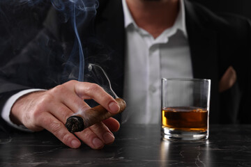 Man with glass of whiskey smoking cigar at dark marble table, closeup - obrazy, fototapety, plakaty