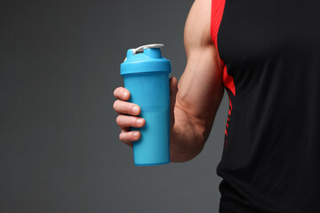 Young man with muscular body holding shaker of protein on grey background, closeup. Space for text