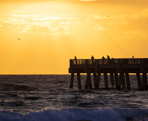 Anglers silhouette against a fiery sunrise at Lake Worth Pier, perfect for themes of leisure and...