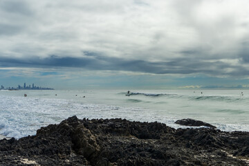 Surfer rides a wave on a rainy day at Currumbin Beach, with Surfers Paradise city skyline on the horizon. Gold Coast, Queensland, Australia.