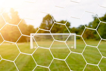 Bright image of a soccer field through the goal net with sun shining on the field