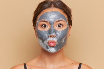 Portrait of young woman with facial mask made from clay posing over studio background, skincare concept, copy space