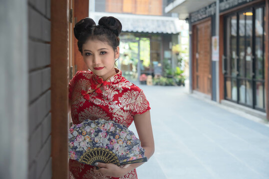 Asian girl wearing a red cheongsam holds a wooden fan in her hand. Pose for photos in Chinatown According to the idea of Chinese New Year