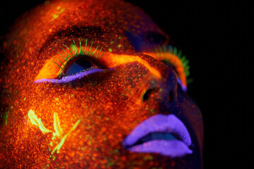Art, woman with neon paint on face and beauty, closeup with bright lipstick and creative skincare on dark background. Orange glow, disco aesthetic and model in studio for creativity with makeup