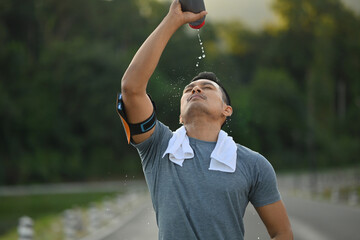 Young athletic man drinking water from a bottle, taking a break from workout in the park.