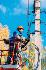 Two professional electricians in hard hats are repairing power lines from cradle of bucket truck. View from below. Electricians change cables on street lighting poles.