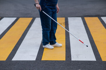 Close-up of the legs of a blind woman crossing the road at a crosswalk with a cane. 