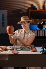 happy female archaeologist holding an antique vase in her hands working late at night in the office...