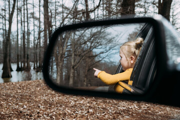 Young child looking out car window pointing at scenery