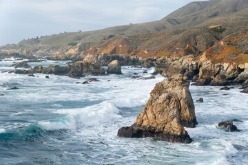 Rocky coast line of Big Sure with wave crashing over seaweed patch