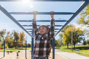 Young boy does monkey bars at playground with bright sun