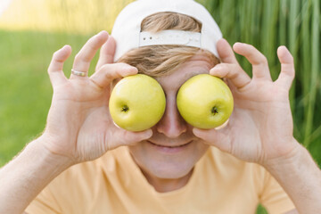 A man fools around with apples, holding them instead of eyes