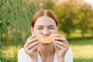 A red-haired woman eats a melon funny, laughs and has fun