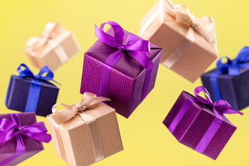 Present. Flying boxes in colored paper tied with a ribbon and a bow on a yellow background. Holidays and greeting cards concept.