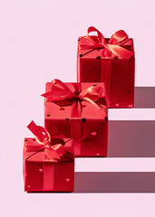 Three gift boxes in Christmas packaging with satin ribbon. Pink background, copy space.