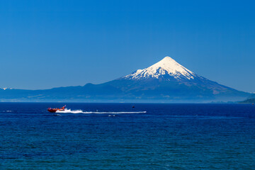 The Osorno Volcano is seen from the banks of Lake Llanquihue, a boat moving in foreground, Puerto...