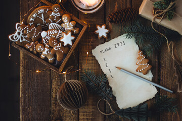 Writing new year resolutions 2025 by hand in December on New Year's Eve. Plan, goals, ideas, projects. Cozy home holiday atmosphere, Christmas lights, festive decor, homemade gingerbread cookies