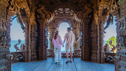 A diverse multiethnic couple of men and women visit The Sanctuary of Truth wooden temple in Pattaya Thailand looking out over the ocean