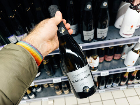 Paris, France - Nov 10, 2023: A hand holds a bottle of Cremant d'Alsace Blanc de Noir, made by Cave de Beblenheim, a choice for a sophisticated sparkling wine
