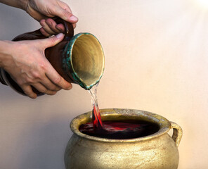 A hand holds a clay jar and pours water - obrazy, fototapety, plakaty
