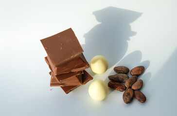 Milk chocolate. White chocolate. Cocoa beans. White background. Sunny shadows.