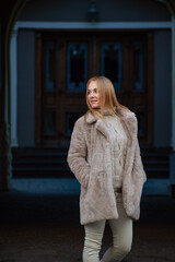 Beautiful woman in light clothes and a fur coat on a city street. Winter season, walk in the city. Vertical frame