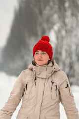 Obraz premium Portrait of beautiful girl in fashionable down jacket and knitted red hat with bubo thoughtfully looking into distance outside in winter