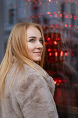 Young blue-eyed attractive woman near of a red store window, Christmas mood. Holiday weekend outdoor. Vertical frame