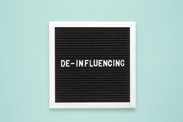 The word deinfluencing on black letter board over isolated blue background