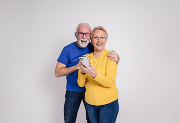Portrait of excited mature husband and wife using mobile phone and laughing on white background