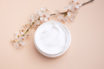 Container with body care and skincare cream on a beage background with blooming cherry. Cosmetic facial skin care and spa. Natural treatment concept.