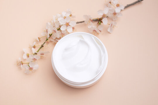 Container with body care and skincare cream on a beage background with blooming cherry. Cosmetic facial skin care and spa. Natural treatment concept.