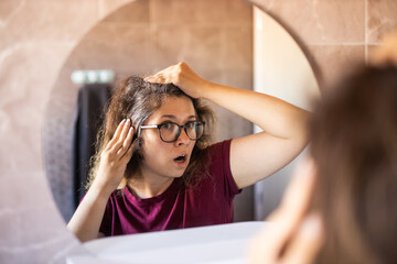 Woman Looking for Gray Hair in the Mirror. Young woman scared of premature aging signs