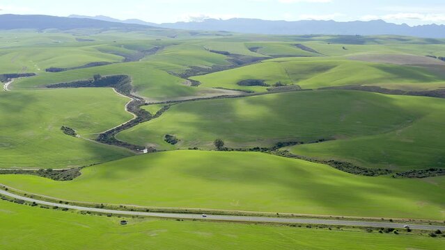 Aerial drone, green grass and road in countryside of natural scenery, greenery and big open fields. View of street, hills and blue sky of peaceful land, rural area or outdoor environment in nature
