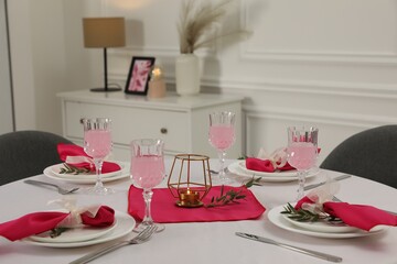 Color accent table setting. Glasses, plates, cutlery and pink napkins on table indoors