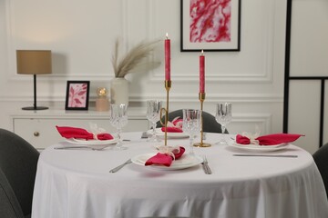 Color accent table setting. Glasses, plates, burning candles and pink napkins on table in dining...